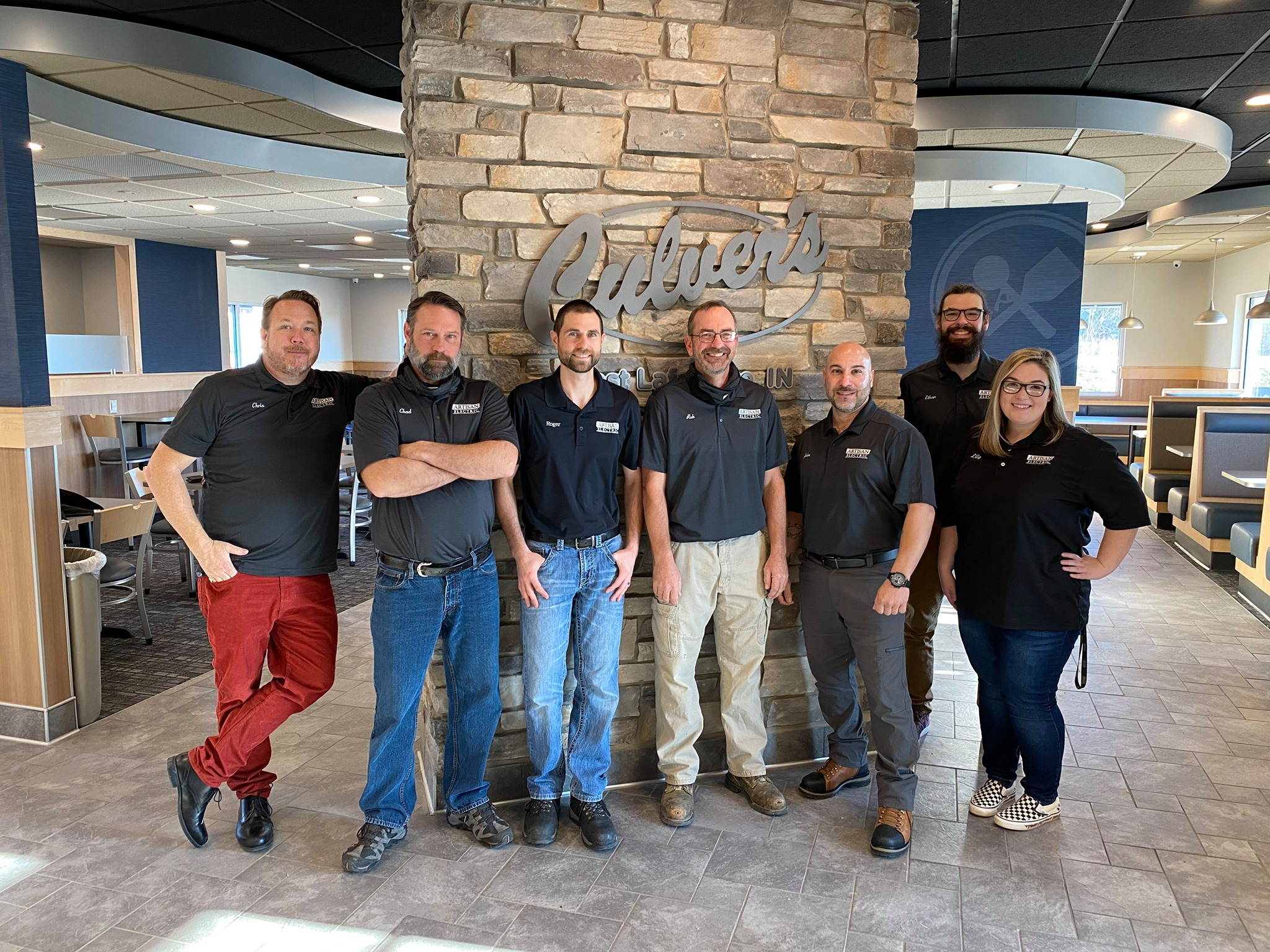Group photo of Artisan Electric team members standing in front of a stone wall in business casual wear. 